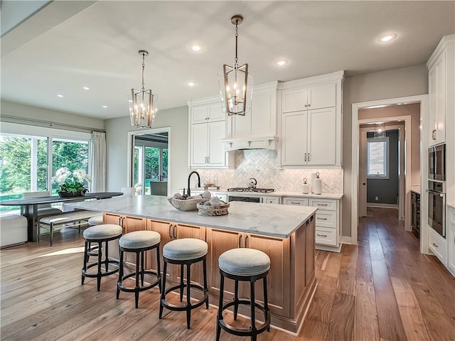 kitchen with a large island with sink, white cabinetry, and decorative light fixtures