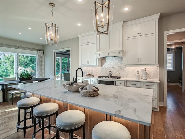 kitchen with a spacious island, light stone counters, hanging light fixtures, and white cabinets