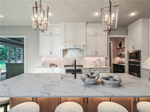 kitchen with white cabinetry, decorative light fixtures, a kitchen island with sink, and stainless steel oven