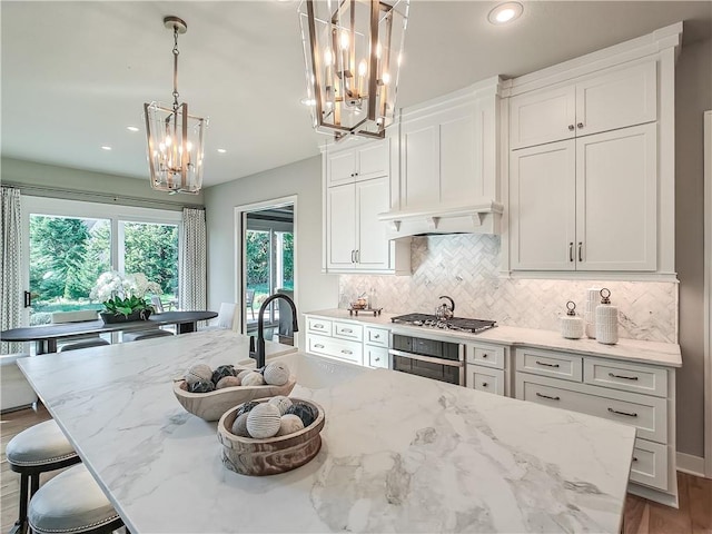 kitchen featuring pendant lighting, a kitchen island with sink, light stone countertops, white cabinets, and oven