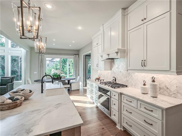 kitchen featuring pendant lighting, light stone countertops, stainless steel appliances, and white cabinets