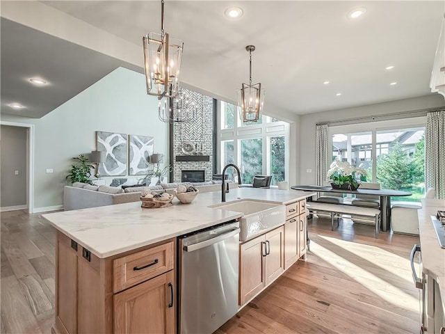 kitchen with a fireplace, dishwasher, sink, light stone counters, and a center island with sink