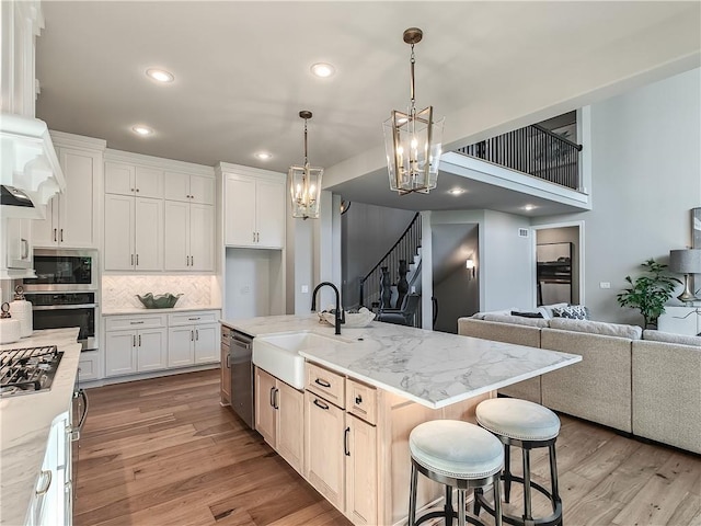 kitchen featuring sink, white cabinetry, appliances with stainless steel finishes, light stone countertops, and a kitchen island with sink