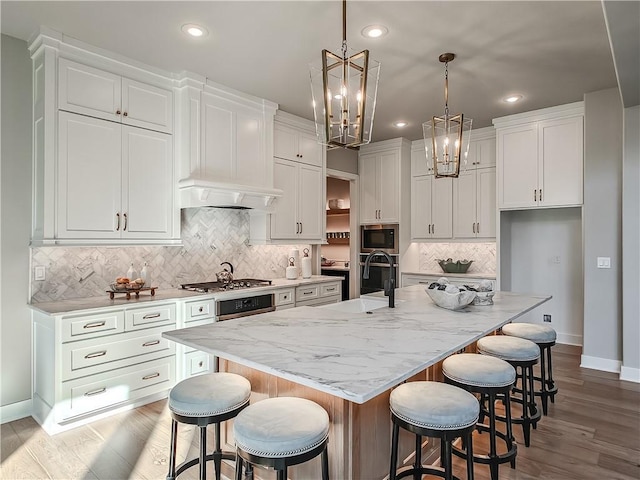 kitchen featuring white cabinets, appliances with stainless steel finishes, a kitchen bar, and a large island with sink