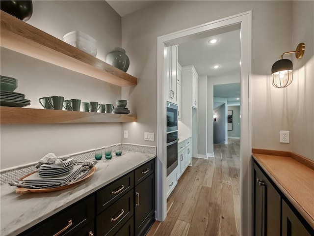 kitchen with white cabinetry, light stone countertops, stainless steel oven, and light hardwood / wood-style flooring