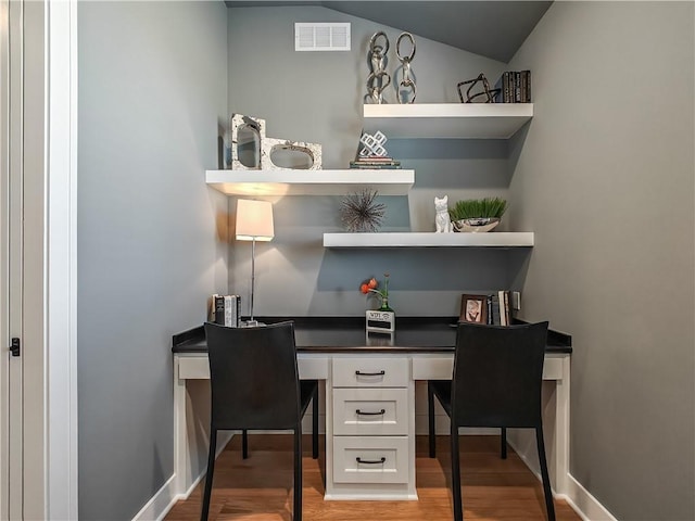 office space featuring hardwood / wood-style flooring, lofted ceiling, and built in desk