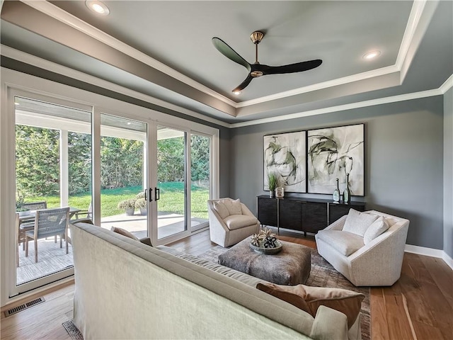 living room featuring wood-type flooring, ornamental molding, ceiling fan, and a tray ceiling