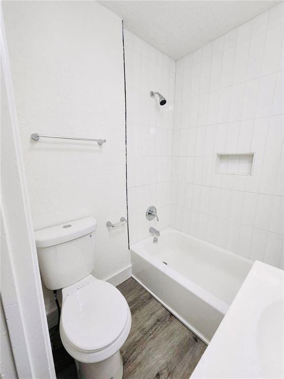 bathroom with tiled shower / bath, wood-type flooring, toilet, and a textured ceiling