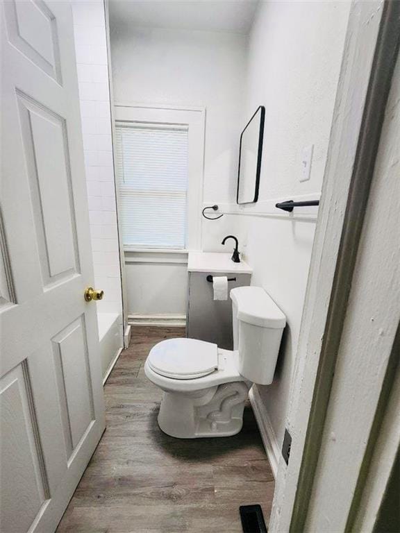 bathroom featuring hardwood / wood-style flooring, a tub to relax in, and toilet