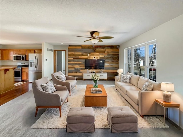 living room with ceiling fan, a textured ceiling, and wood walls