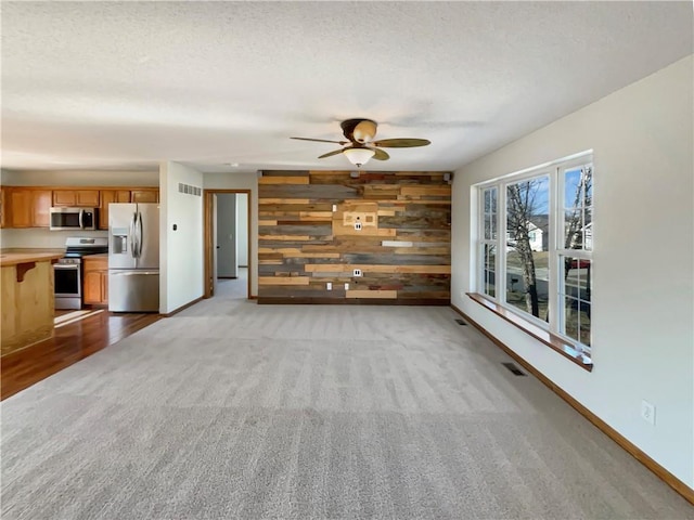 unfurnished living room featuring ceiling fan, light colored carpet, a textured ceiling, and wood walls