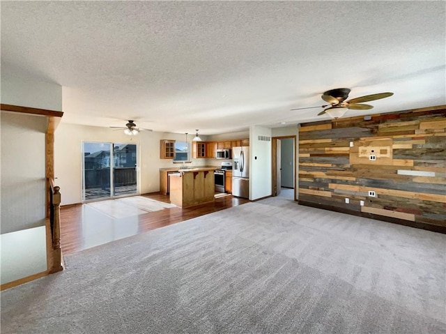 unfurnished living room with light carpet, ceiling fan, a textured ceiling, and wood walls