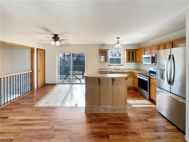 kitchen featuring sink, appliances with stainless steel finishes, light hardwood / wood-style floors, a kitchen island, and decorative light fixtures