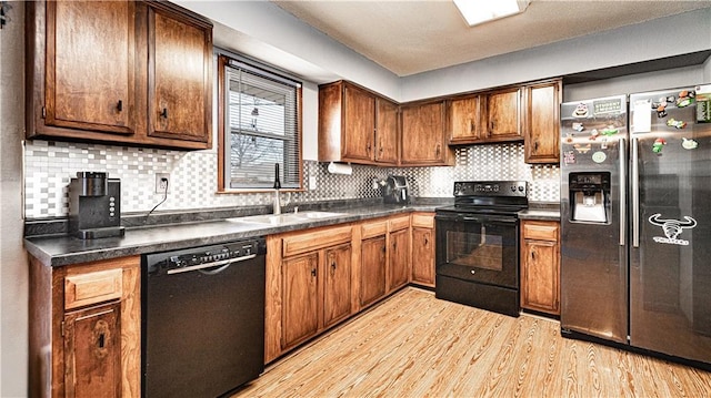 kitchen featuring decorative backsplash, light wood-style floors, dark countertops, black appliances, and a sink