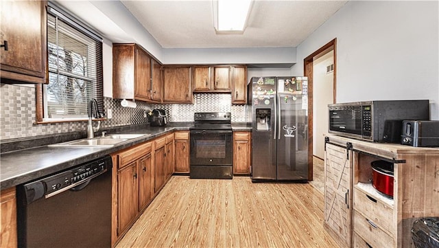 kitchen featuring dark countertops, a sink, light wood-style flooring, and black appliances