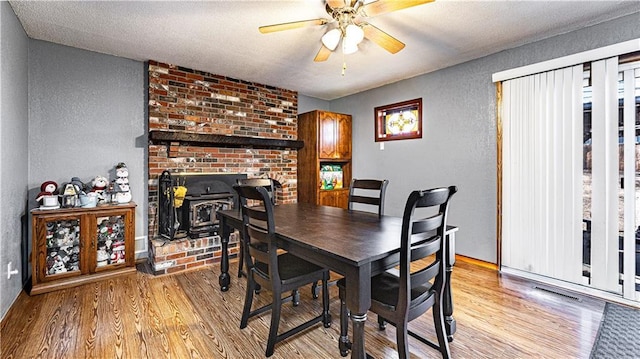 dining room with ceiling fan, a textured wall, a textured ceiling, light wood-style floors, and a wood stove