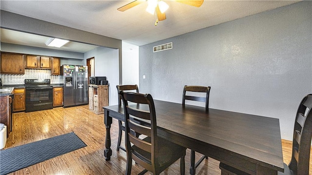 dining room featuring a ceiling fan, visible vents, a textured wall, and light wood finished floors