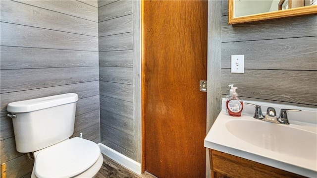 half bathroom featuring toilet, wooden walls, and vanity