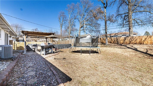 view of yard featuring a trampoline, central AC, and a fenced backyard