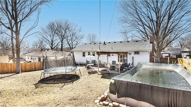 back of property with a patio area, a fenced backyard, a trampoline, and a fire pit