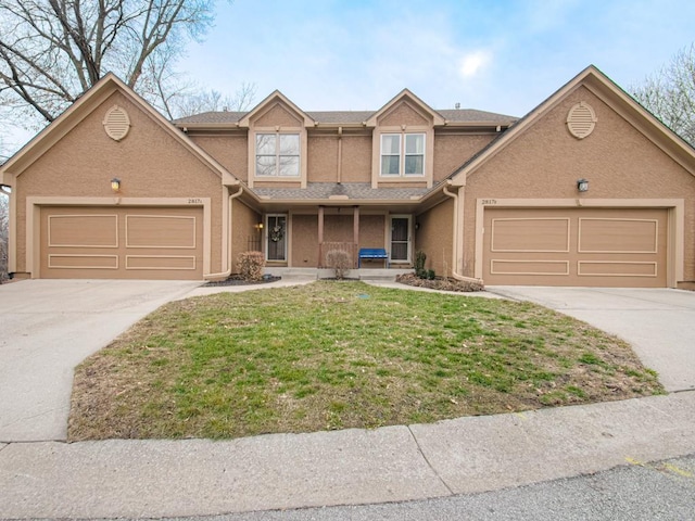 traditional-style house featuring a garage, driveway, a front lawn, and stucco siding