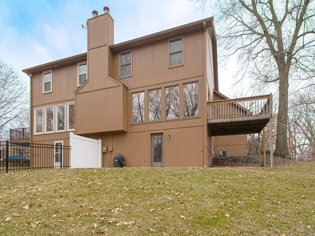 rear view of property with a chimney, a wooden deck, and a lawn