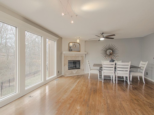 unfurnished dining area featuring baseboards, ceiling fan, a premium fireplace, and wood finished floors