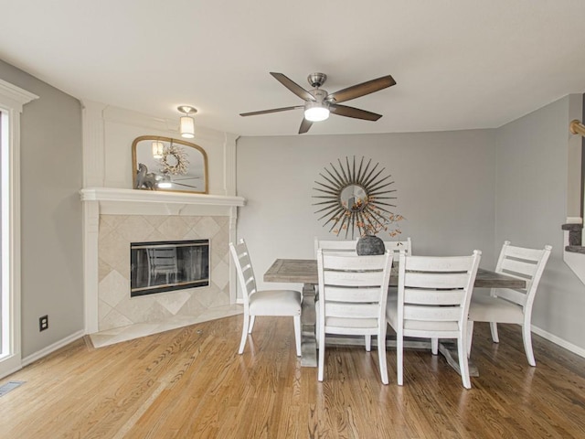 unfurnished dining area with a ceiling fan, baseboards, a tiled fireplace, and wood finished floors