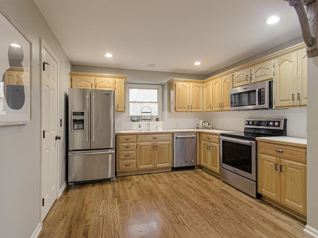 kitchen with light brown cabinets, a sink, light countertops, appliances with stainless steel finishes, and light wood finished floors