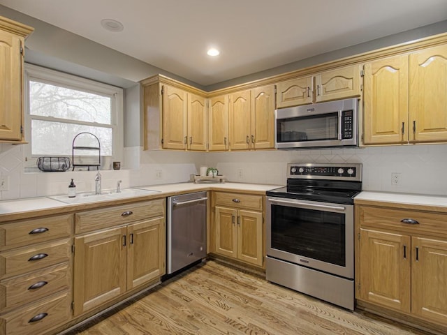 kitchen featuring light wood-style floors, appliances with stainless steel finishes, light countertops, and a sink