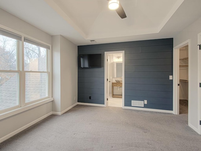 empty room with ceiling fan, light carpet, visible vents, baseboards, and a raised ceiling