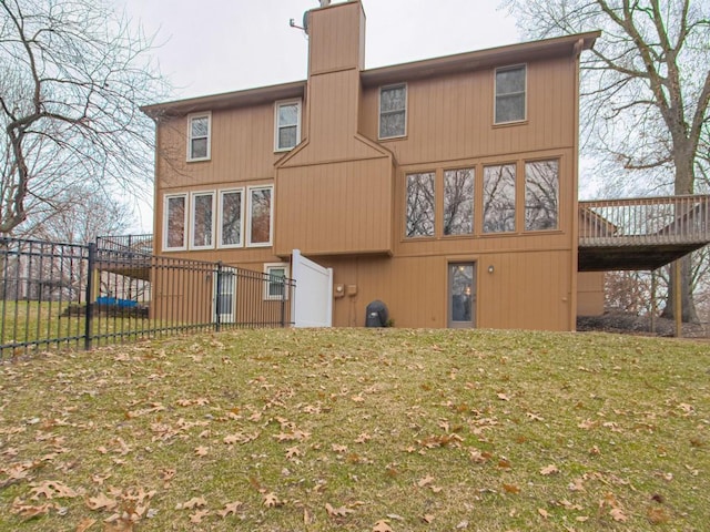 rear view of house featuring a chimney, fence, a lawn, and a wooden deck