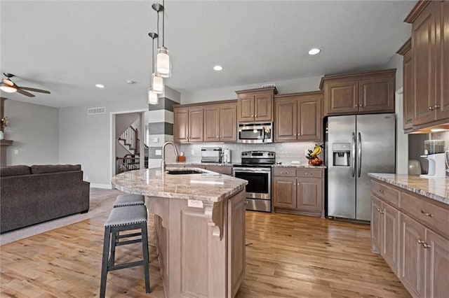 kitchen with appliances with stainless steel finishes, a breakfast bar area, light stone countertops, sink, and a kitchen island with sink