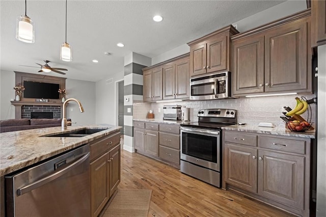 kitchen featuring light wood-type flooring, a brick fireplace, sink, tasteful backsplash, and appliances with stainless steel finishes