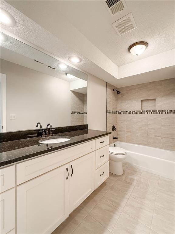 full bathroom with toilet, vanity, tiled shower / bath, and a textured ceiling