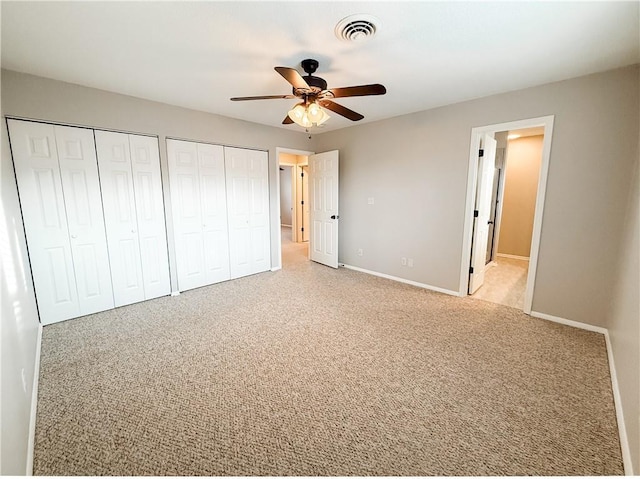 unfurnished bedroom with light carpet, two closets, and ceiling fan