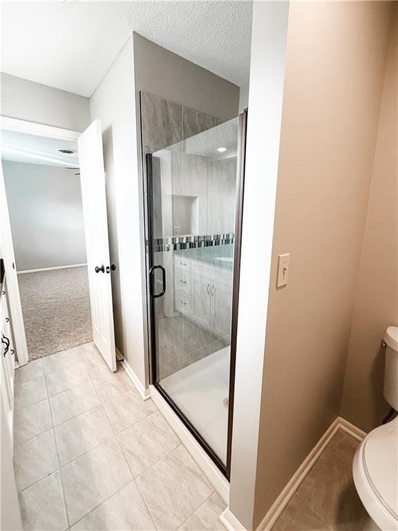 bathroom featuring tile patterned flooring, a shower with door, toilet, and a textured ceiling