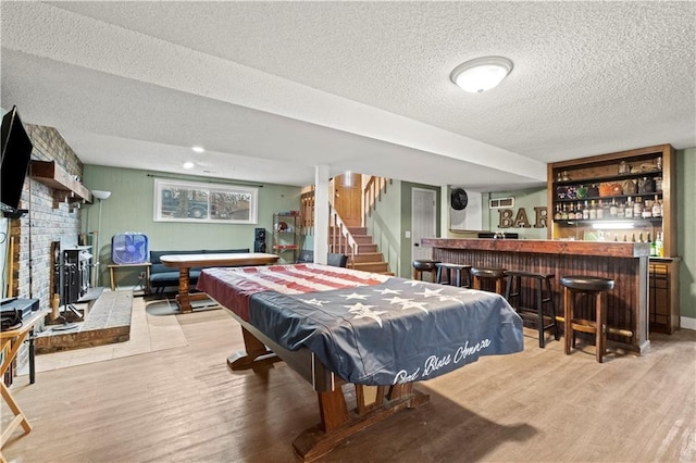 playroom featuring billiards, a brick fireplace, bar area, a textured ceiling, and light hardwood / wood-style flooring