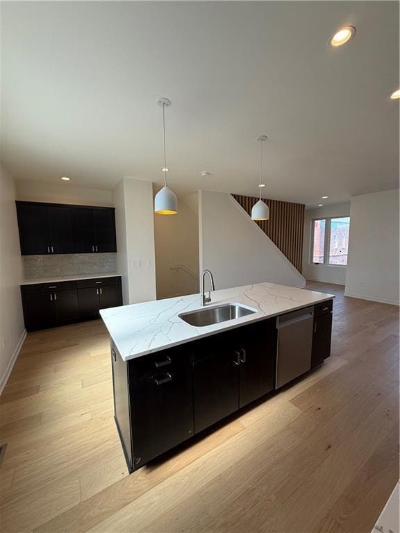 kitchen featuring light wood-style flooring, stainless steel dishwasher, dark cabinetry, and a sink