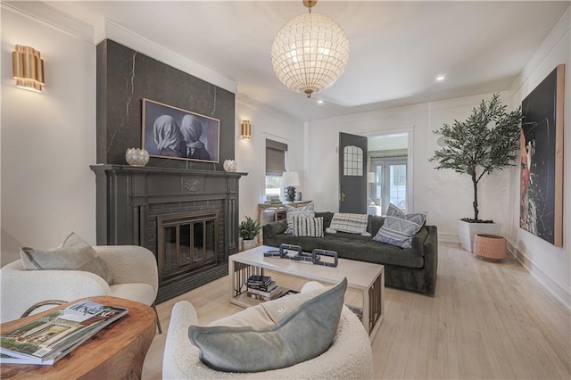 living area featuring baseboards, light wood finished floors, ornamental molding, a brick fireplace, and a notable chandelier