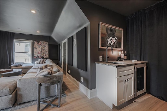 bar featuring lofted ceiling, a sink, wet bar, light wood finished floors, and baseboards