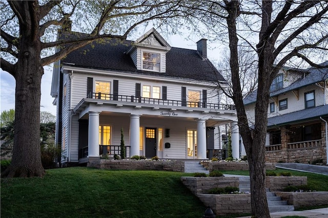 view of front of house featuring a front lawn, a balcony, covered porch, and a chimney