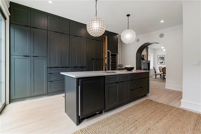 kitchen with light wood finished floors, decorative light fixtures, light countertops, arched walkways, and a sink