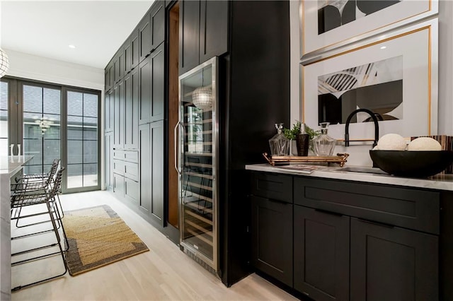 kitchen with beverage cooler, a sink, light countertops, light wood-style floors, and dark cabinets