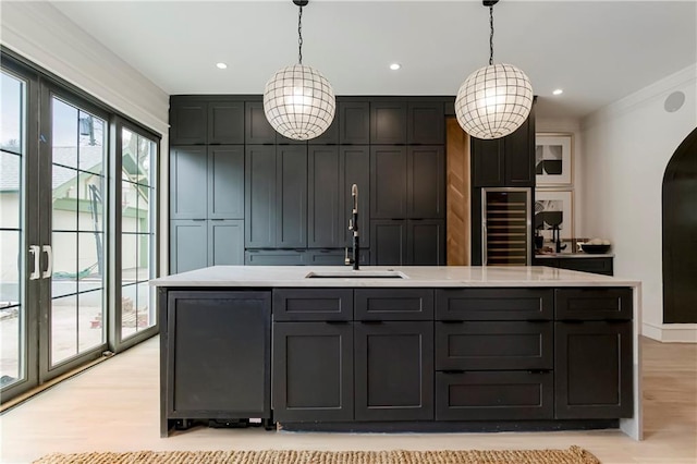 kitchen featuring an island with sink, arched walkways, a sink, light countertops, and light wood-style floors