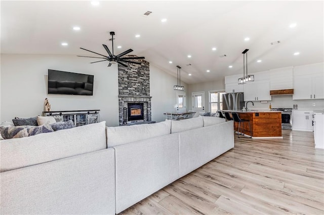 living room with high vaulted ceiling, a stone fireplace, sink, and light wood-type flooring