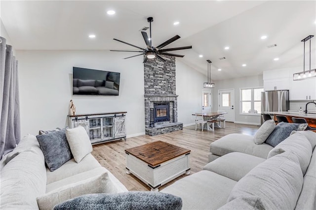 living room featuring ceiling fan, sink, a stone fireplace, and light hardwood / wood-style floors