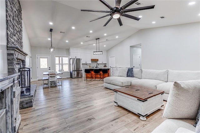 living room with lofted ceiling, sink, ceiling fan, a fireplace, and light wood-type flooring