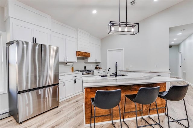 kitchen featuring a kitchen island with sink, sink, light stone countertops, and stainless steel refrigerator