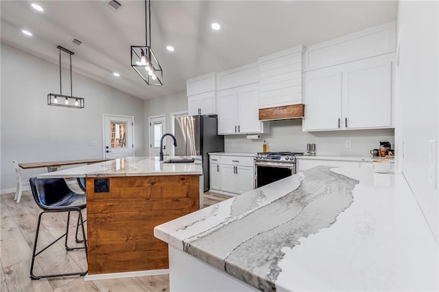 kitchen featuring hanging light fixtures, appliances with stainless steel finishes, white cabinets, and a center island with sink